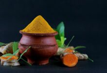 مسحوق الكركم الأصفر في وعاء خشبي مع جذور الكركم الطازجة